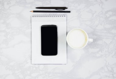 Mermer bir masada telefon, not defteri, yazı kalemi ve bir fincan kahve içeren işyeri. Üst görünüm, düz döşeme, kopyalama alanı