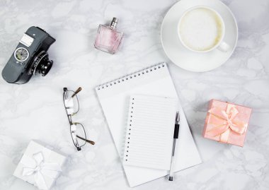 Not defteri, parfüm, kalem, gözlük, kamera, hediye kutusu ve mermer bir masa üzerinde bir fincan kahve ile işyeri. Üst görünüm, düz döşeme, kopyalama alanı