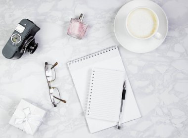 Not defteri, parfüm, kalem, gözlük, kamera, hediye kutusu ve mermer bir masa üzerinde bir fincan kahve ile işyeri. Üst görünüm, düz döşeme, kopyalama alanı