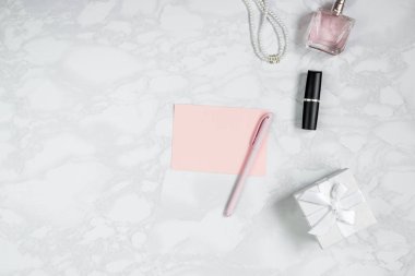 Beyaz mermer masa üzerinde kadın aksesuarları. Pembe kağıt, pembe kalem, parfüm, hediye kutusu, inci, ruj. Etiket eklemek için düzen. Üst görünüm, düz döşeme, kopyalama alanı
