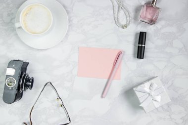 Beyaz mermer bir masada kadın aksesuarları. Pembe bir kağıt, kalem, defter, parfüm, hediye kutusu, inci, gözlük, bir bardak kahve ve diğer kadın aksesuarları. Etiket eklemek için düzen. Düz yatıyordu