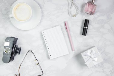 Beyaz mermer bir masada kadın aksesuarları. Kağıt, kalem, defter, parfüm, hediye kutusu, inci, gözlük, bir bardak kahve ve diğer kadın aksesuarları pembe bir levha. Etiket eklemek için düzen. Düz yatıyordu