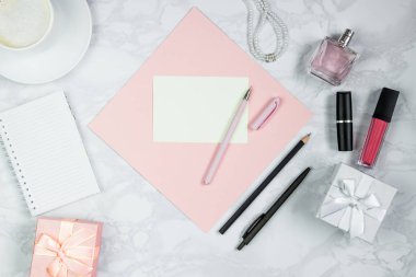 Beyaz mermer masaüzerinde kadın aksesuarları. Pembe bir kağıt, kalem, defter, parfüm, hediye kutusu, inci, bir bardak kahve ve diğer kadın kozmetikleri. Etiket eklemek için düzen. Düz döşeme, kopyalama alanı