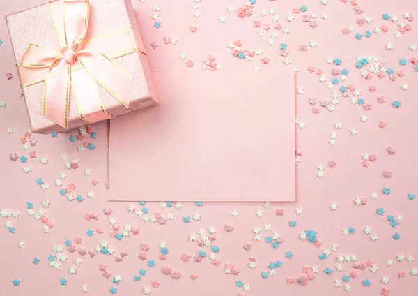 Layout for recording. Pink sheet for writing and a gift box on a pink background with decorative multi-colored elements with stars and bows. Flat lay, top view