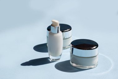 Yüz estetiği. Mavi arka planda koyu gölgeli kavanozlar, serum ve yüz maskesi. Güzellik blogcusu, prosedür salonu konsepti. Minimalizm.
