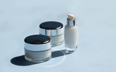 Yüz estetiği. Mavi arka planda koyu gölgeli kavanozlar, serum ve yüz maskesi. Güzellik blogcusu, prosedür salonu konsepti. Minimalizm.