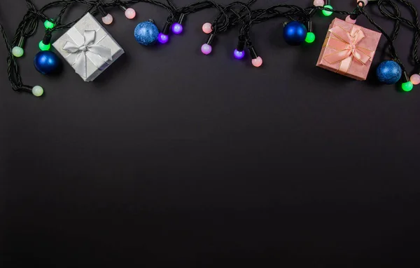 Hermosa composición de Navidad sobre un fondo negro con cajas de regalo de Navidad y brillantes luces de guirnalda multicolor. Vista desde arriba. Copiar espacio — Foto de Stock