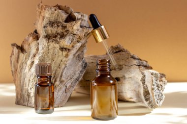 Parlak güneş ışığıyla bej bir arka planda bir kütüğün yanında duran cam kozmetik şişeleri. Doğal kozmetik kavramı, doğal temel petrol..