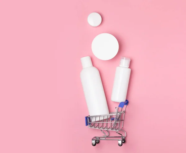 White cosmetic jars lie in a shopping basket on a pink background. Online home shopping. Purchase of disinfection, laundry and care products. — Stock Photo, Image