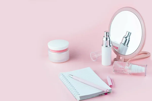 Face care cosmetics. Jars of cream and face serum and notes for writing on a pink background