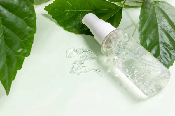 Glass cosmetic bottles with a dropper stand next to green leaves on a white background. Organic cosmetics concept, natural essential oil and cream