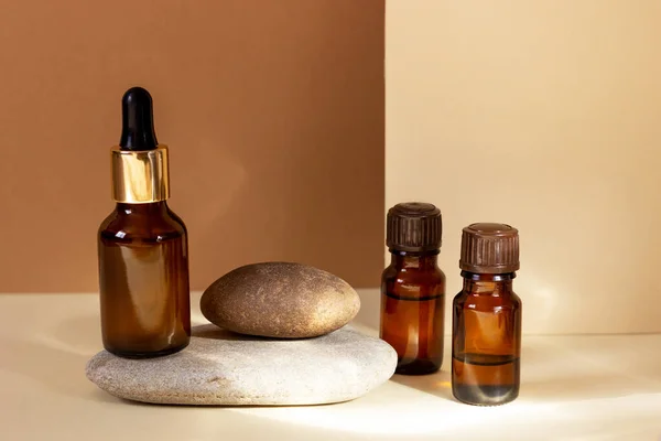 Glas cosmetische flessen met een druppelaar staan naast een log op een beige achtergrond met fel zonlicht. Het concept van natuurlijke cosmetica, natuurlijke essentiële olie. — Stockfoto
