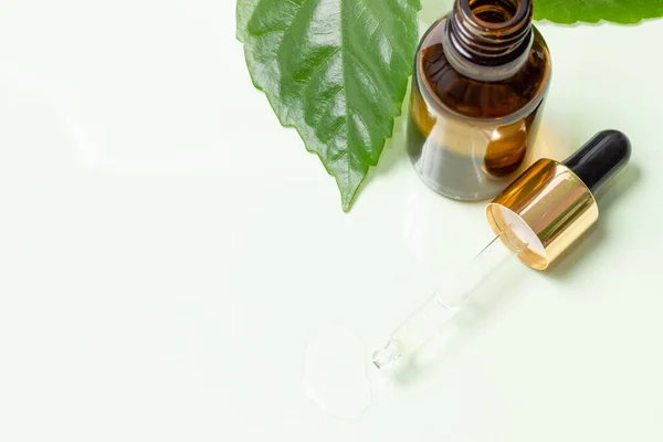 Glass cosmetic bottles with a dropper stand next to green leaves on a white background. Organic cosmetics concept, natural essential oil and cream