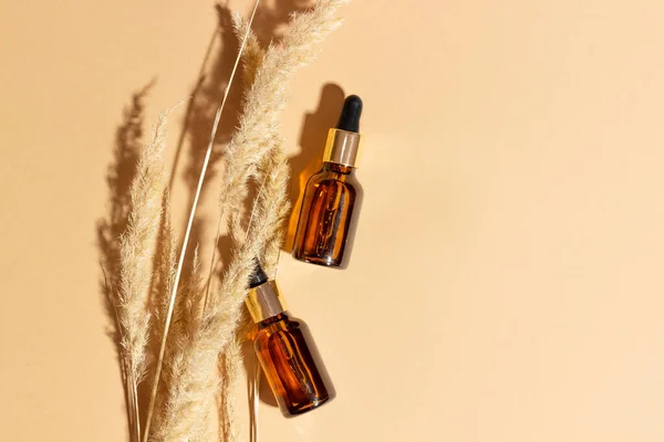 Natural cosmetics in glass bottles with a dropper on a beige background with branches. The concept of natural cosmetics, natural essential oil.