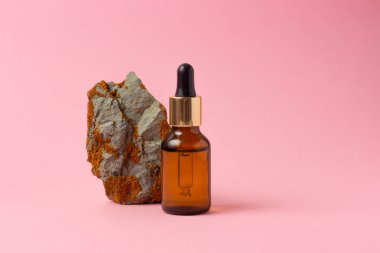 Gerekli yağlar ve kozmetik ürünleri için kehribar bir şişe taşın yanında duruyor. Pembe arka planda cam şişe. Damla, sprey şişesi. Doğal kozmetik konsepti.