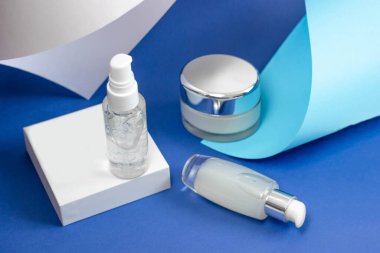 Serum, jöle ve mavi arka planda yüz kremi olan kozmetik şişeleri. Deri kozmetiği, minimalizm. Salon prosedürleri kavramı.