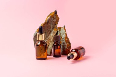 Gerekli yağlar ve kozmetik ürünleri için kehribar bir şişe taşın yanında duruyor. Pembe arka planda cam şişe. Damla, sprey şişesi. Doğal kozmetik konsepti.