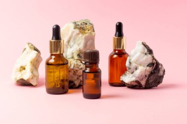 Gerekli yağlar ve kozmetik ürünleri için kehribar bir şişe taşın yanında duruyor. Pembe arka planda cam şişe. Damla, sprey şişesi. Doğal kozmetik konsepti.