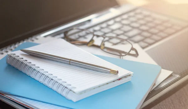 Workplace with laptop, notebook and glasses on a wooden table. Work from home. Blurred background.