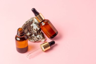 Gerekli yağlar ve kozmetik ürünleri için kehribar bir şişe taşın yanında duruyor. Pembe arka planda cam şişe. Damla, sprey şişesi. Doğal kozmetik konsepti.