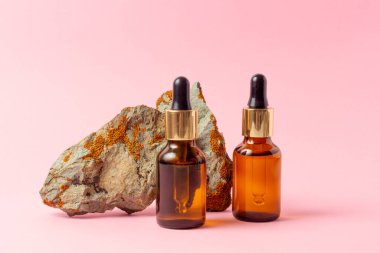 Gerekli yağlar ve kozmetik ürünleri için kehribar bir şişe taşın yanında duruyor. Pembe arka planda cam şişe. Damla, sprey şişesi. Doğal kozmetik konsepti.