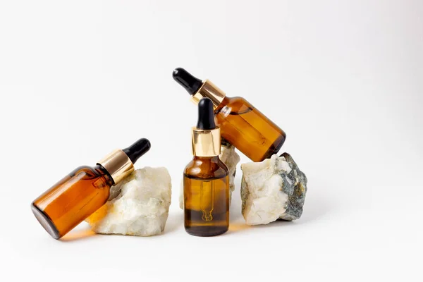 Natural cosmetics in glass bottles with a dropper stand next to a stone on a beige background with bright sunlight. The concept of natural cosmetics, natural essential oil