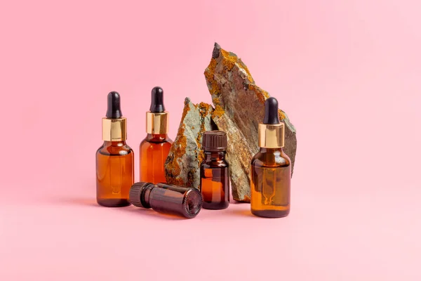 An amber bottle for essential oils and cosmetics stands next to the stone. Glass bottle on a pink background. Dropper, spray bottle. Natural cosmetics concept.