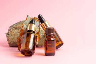 Gerekli yağlar ve kozmetik ürünleri için kehribar bir şişe taşın yanında duruyor. Pembe arka planda cam şişe. Damla, sprey şişesi. Doğal kozmetik konsepti.