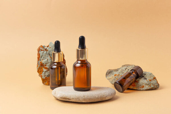 Рядом с камнем стоит янтарная бутылка для эфирных масел и косметики. Стеклянная бутылка. Капельница, баллончик. Концепция натуральной косметики.