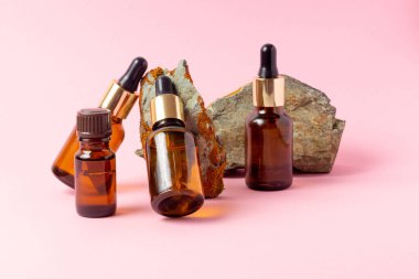 Gerekli yağlar ve kozmetik ürünleri için kehribar bir şişe taşın yanında duruyor. Pembe arka planda cam şişe. Damla, sprey şişesi. Doğal kozmetik konsepti.