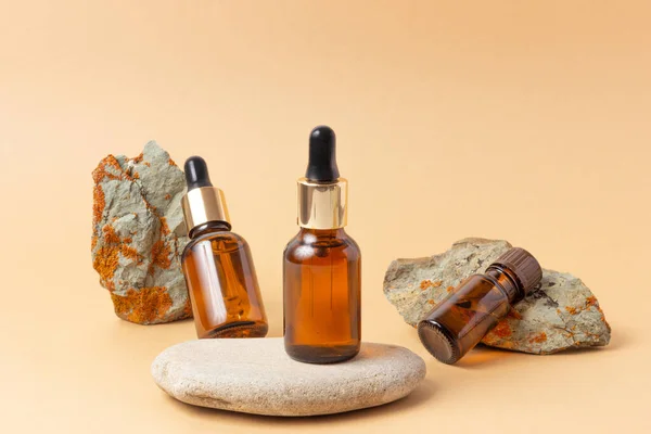 An amber bottle for essential oils and cosmetics stands next to the stone. Glass bottle on a pink background. Dropper, spray bottle. Natural cosmetics concept.