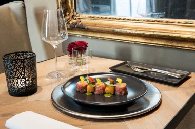 Gurme deniz ürünleri lezzetleri ile tabak mum, çiçek ve bardağı ile resmi bir masada çiğ balık yaprak garnitür ile servis fileto haddelenmiş