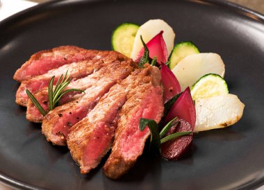 Lezzetli orta ham rosemary ile süslenmiş ve kabak ve siyah bir tabak patates gibi sebzeler ile servis biftek dilimlenmiş