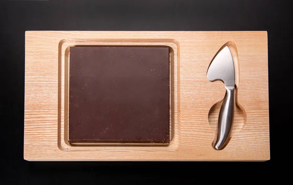 平板牛奶巧克力的目的是用不锈钢刀或刀从上面观看黑色背景的木制板 — 图库照片