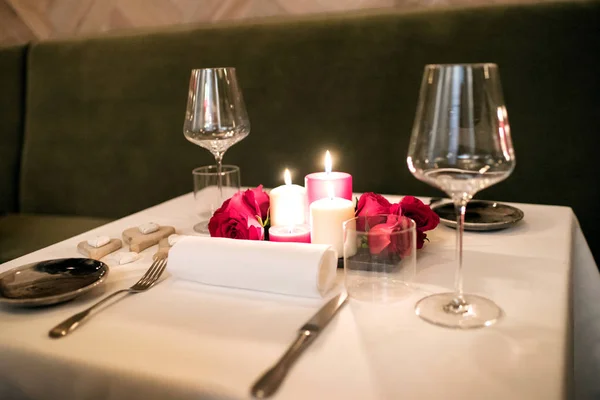 Intimate romantic table setting by candlelight for two with a centrepiece of burning candles and red rose petals and elegant dinnerware for a Valentines or anniversary celebration
