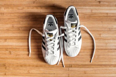 Adidas Superstar spor ayakkabı ikonik üç mavi çizgili bir ahşap zemin üzerinde üstten geri bağcıklarımı ile görüntülendi.