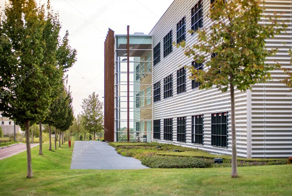 Modern office block with landscaped garden, green lawn and trees and a glazed multi-storey extension