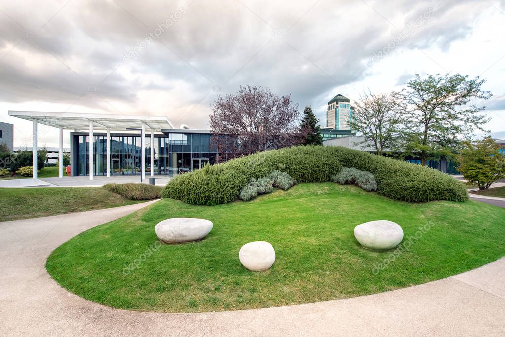 Landscaped traffic island by road outside modern building.