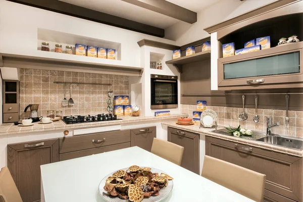 Rustic or kitchen interior with cooking supplies, built in cabinets with tiled splash back, fitted appliances and a center table with homemade cookies