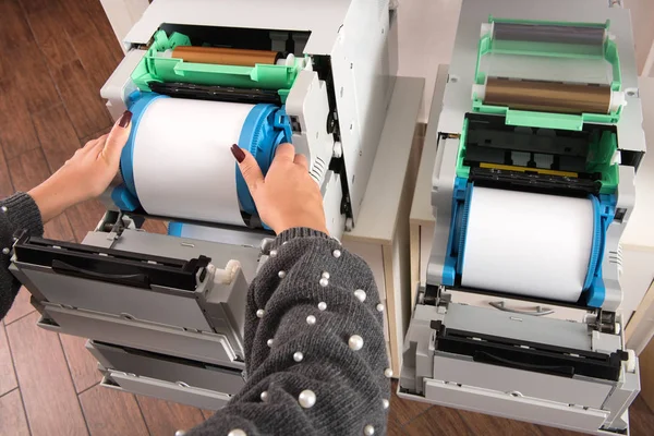 Woman placing a new roll of photographic film paper in a printer in a photographic studio or printing house in a close up view of her hands