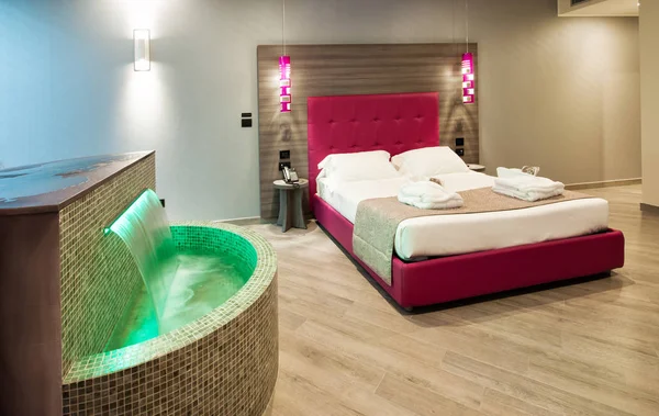 Modern motel bedroom in a luxury suite with green tiled water feature and a double bed with illuminated lamps and headboard