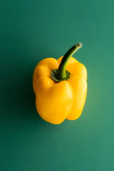 One whole yellow sweet pepper on green background, viewed from above in close-up