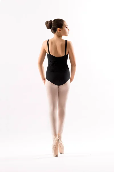 一个年轻的芭蕾演员穿着黑色紧身衣 在她的脚趾尖上摆姿势平衡 她的后路是在白色上被隔离的 — 图库照片