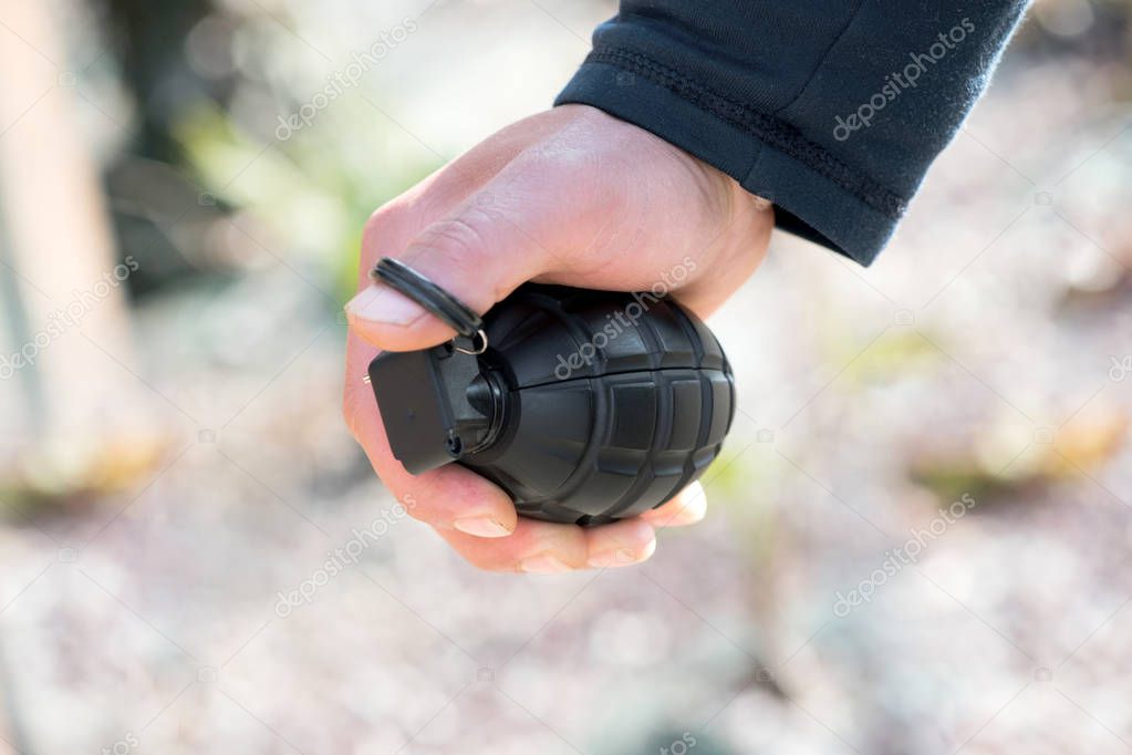 Man clutching a grenade in his hand with his thumb through the ring of the pin in a concept of terrorism or war