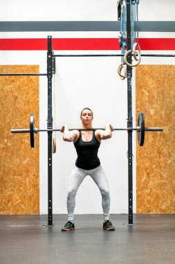 Genç bir kadın spor salonunda çömeliyor.