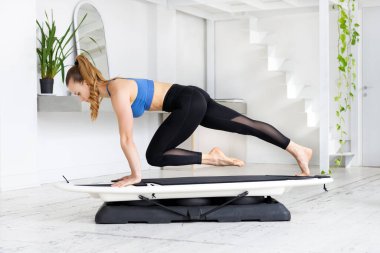 Genç bir kadın, sağlık ve zindelik konseptinde yüksek bir spor salonunda kardiyovasküler egzersizle sörf tahtasında sörf yapıyor.