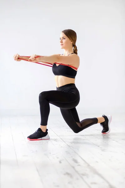 Woman doing a power band behind lunge and forward push exercise to strengthen her core muscles using resistance in a high key gym with copyspace in a health and fitness concept
