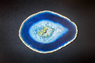 İnce dilimlenmiş mavi agat dilimi, tepede düz bir manzarada, siyah bir masanın üzerinde yatıyordu.