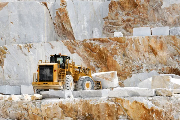 Heavy duty front end loader moving marble blocks inside an open cast quarry in Tuscany Italy excavating white Carrara marble