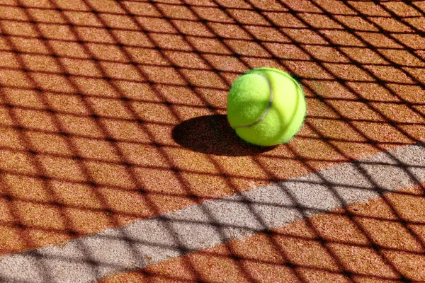 Green tennis ball on an outdoor court with white line marking and pattern of the shadow cast by the net, with copyspace